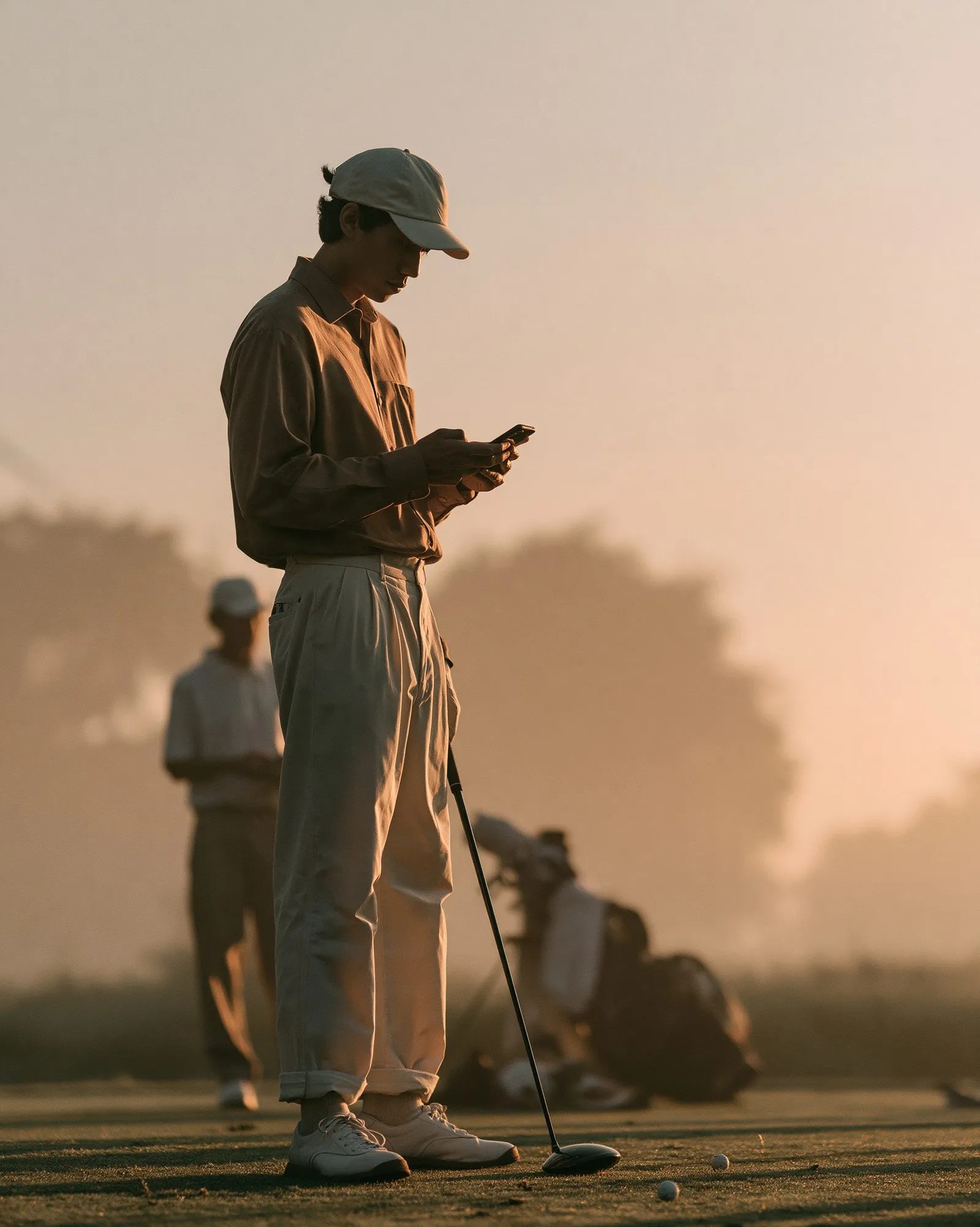 A golfer on a tee box at first light, checking the phone before the round