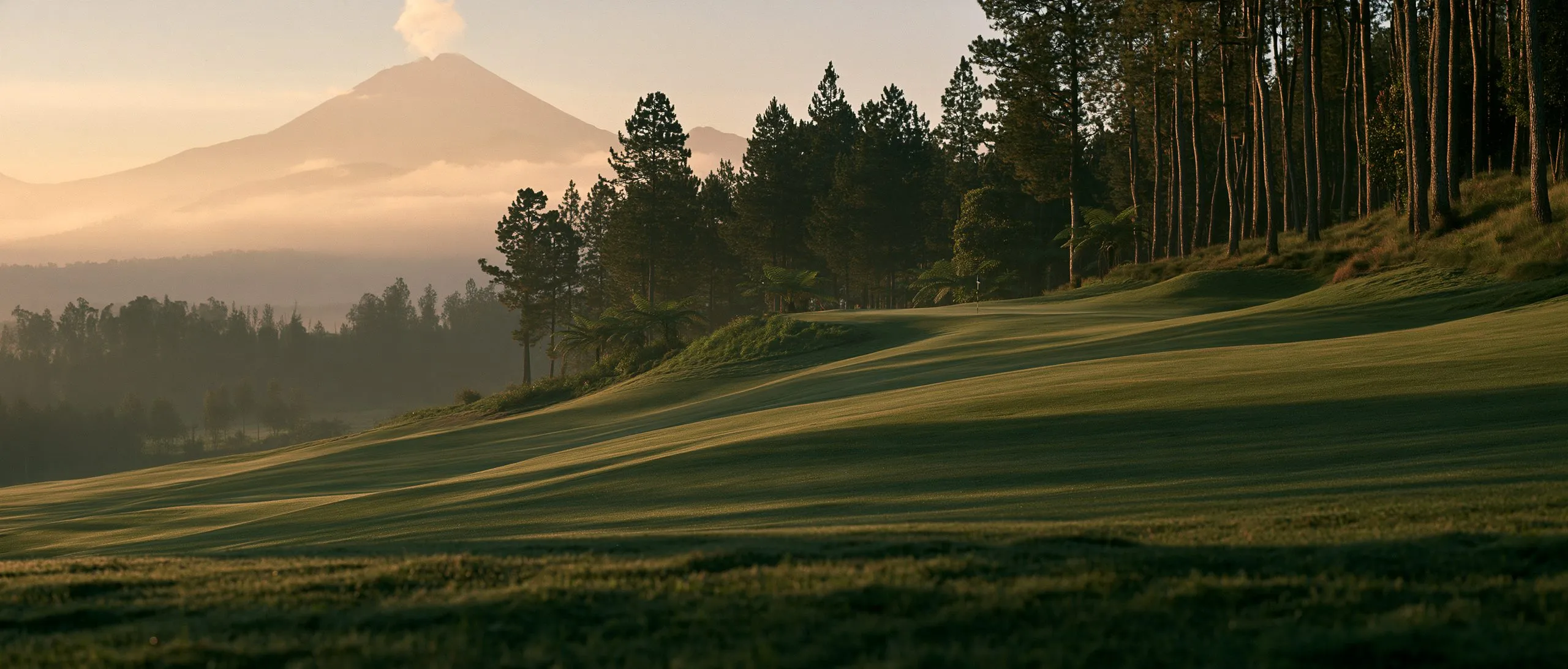 A highland golf course at dawn, mist over the fairway and a volcano on the horizon